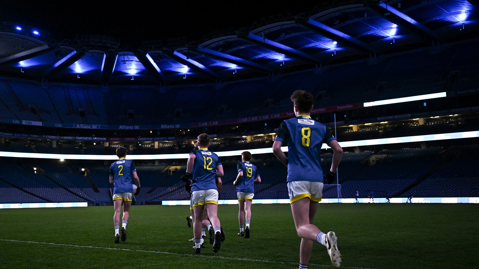 Players entering Croke Park’s pitch beneath blue stadium bowl lighting
