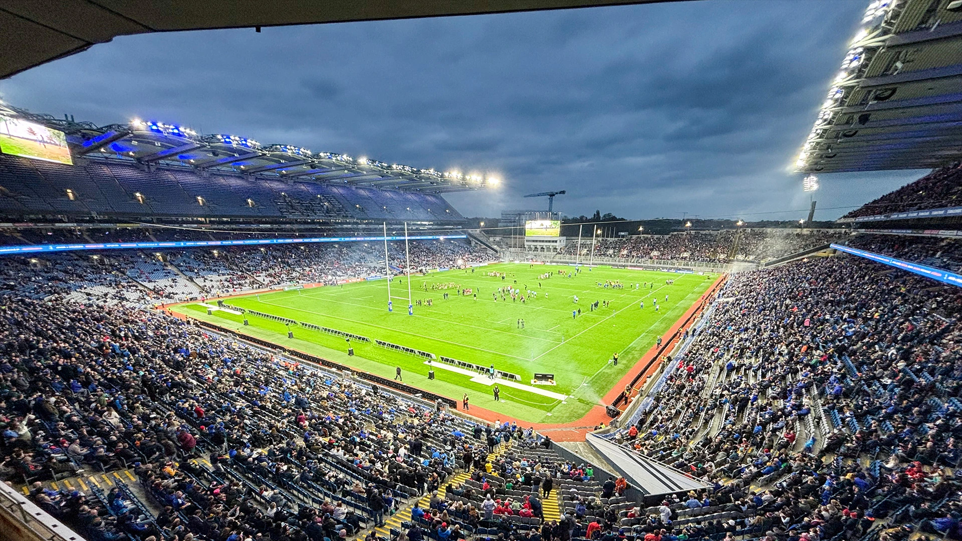 Croke Park stadium at dusk with floodlights illuminating the pitch and spectator stands