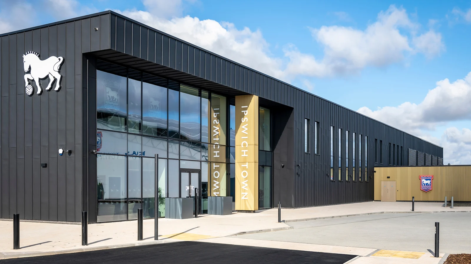 The entrance to Ipswich Town FC’s completed training complex, with dark cladding, glazing and club branding.