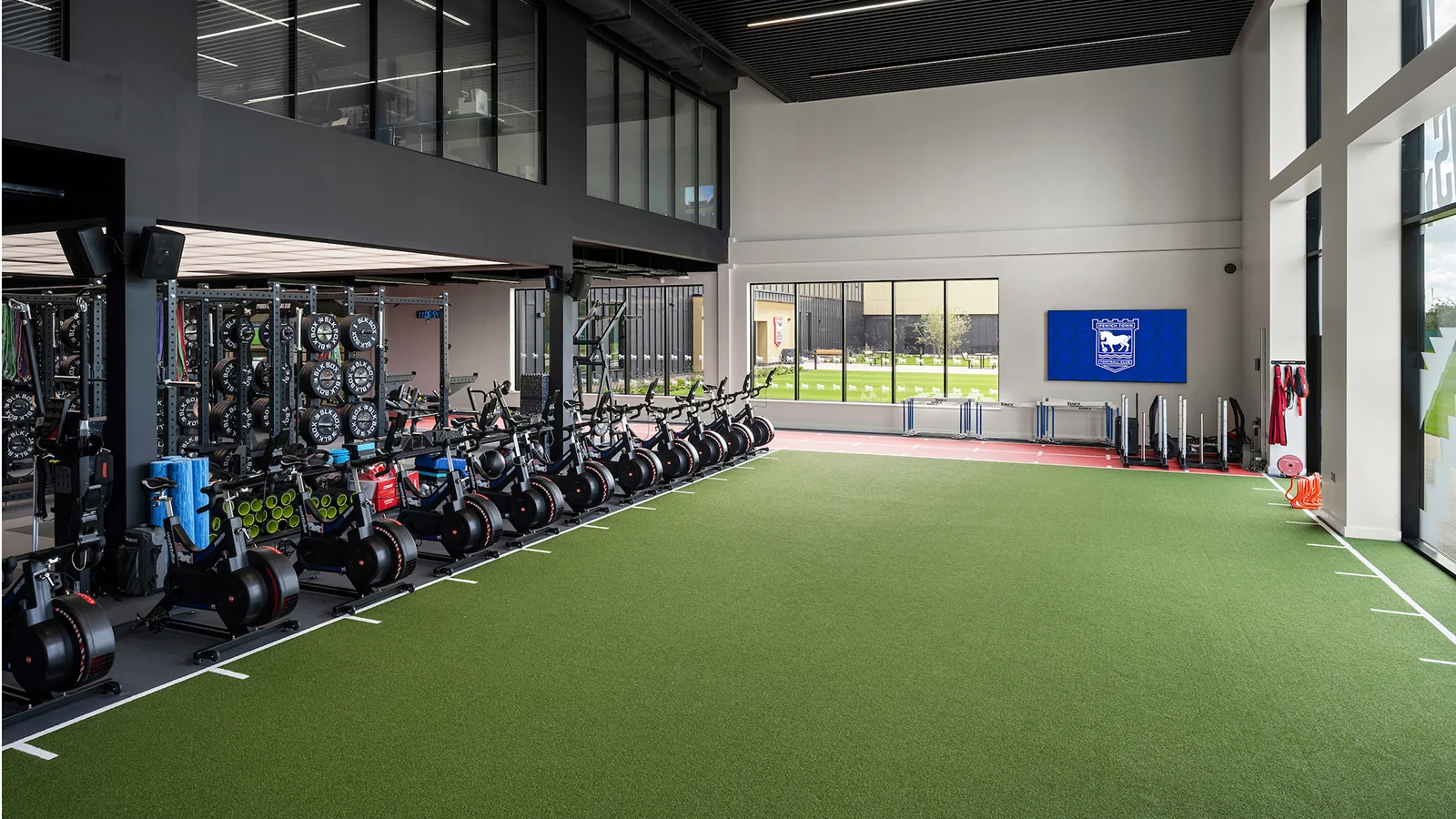 The double-height training gym with exercise equipment, an indoor turf area and full-height glazing.