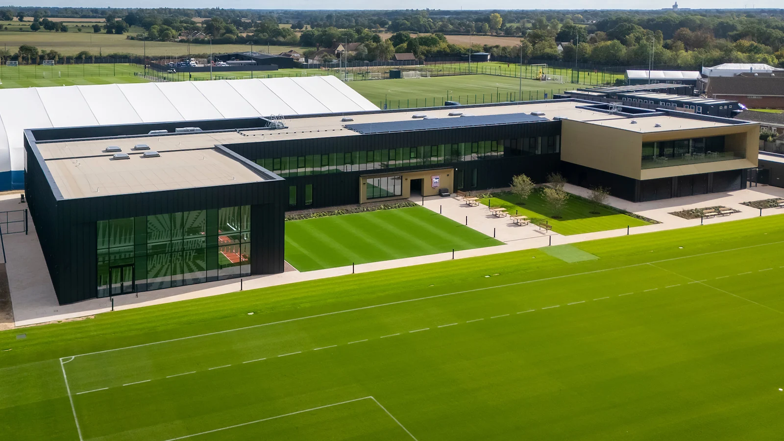 An aerial view of the completed training building beside the pitches, showing its courtyard and roof-mounted solar panels.